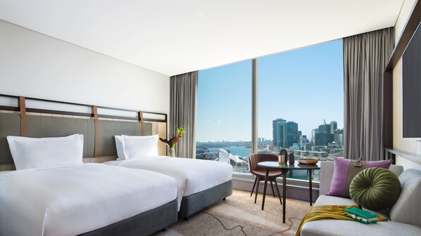Habitación de hotel con dos camas, un sofá, una mesita y vistas a la silueta de la ciudad.