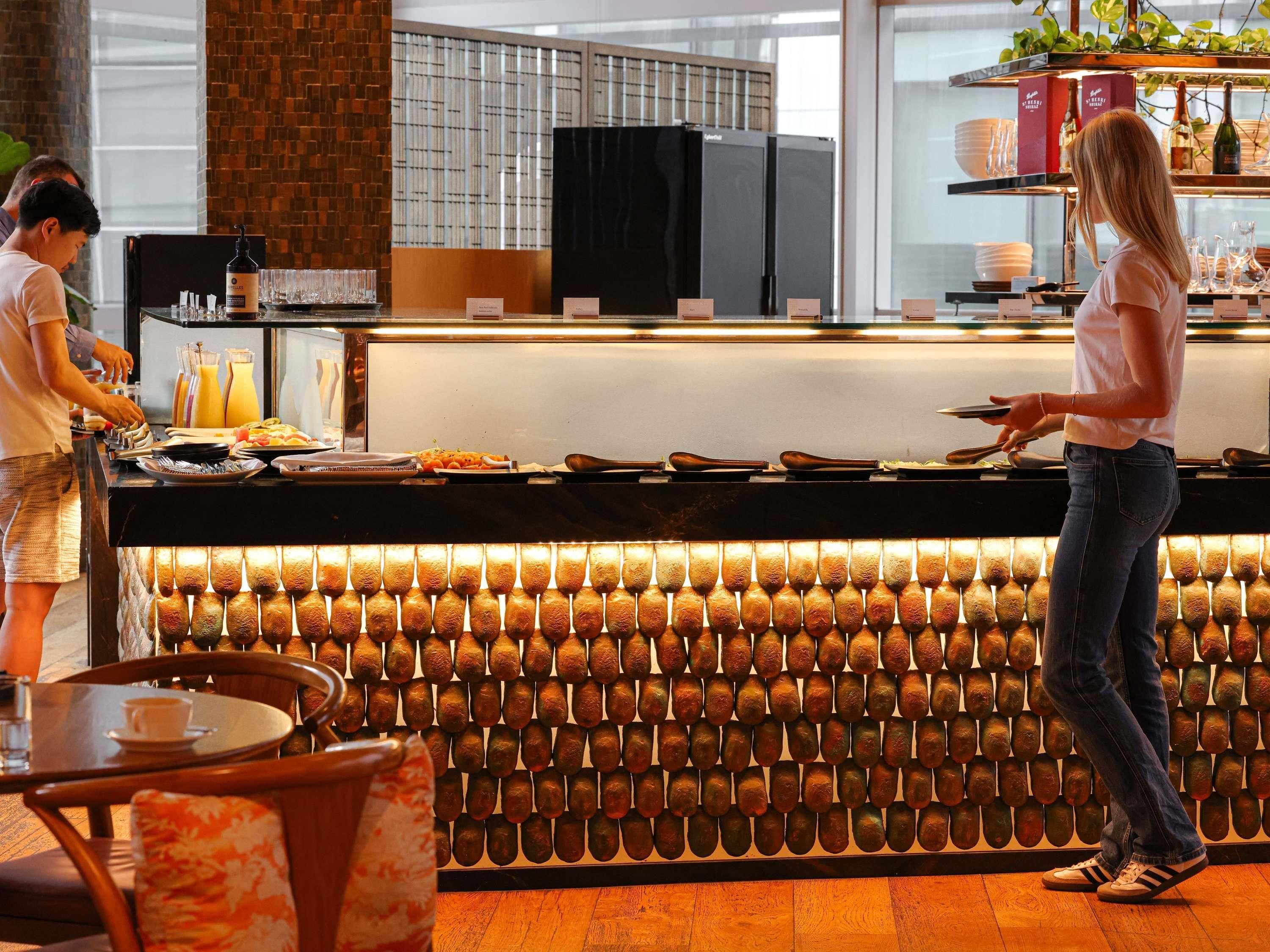 A breakfast bar with a variety of food items and a counter where a server is attending to a guest.