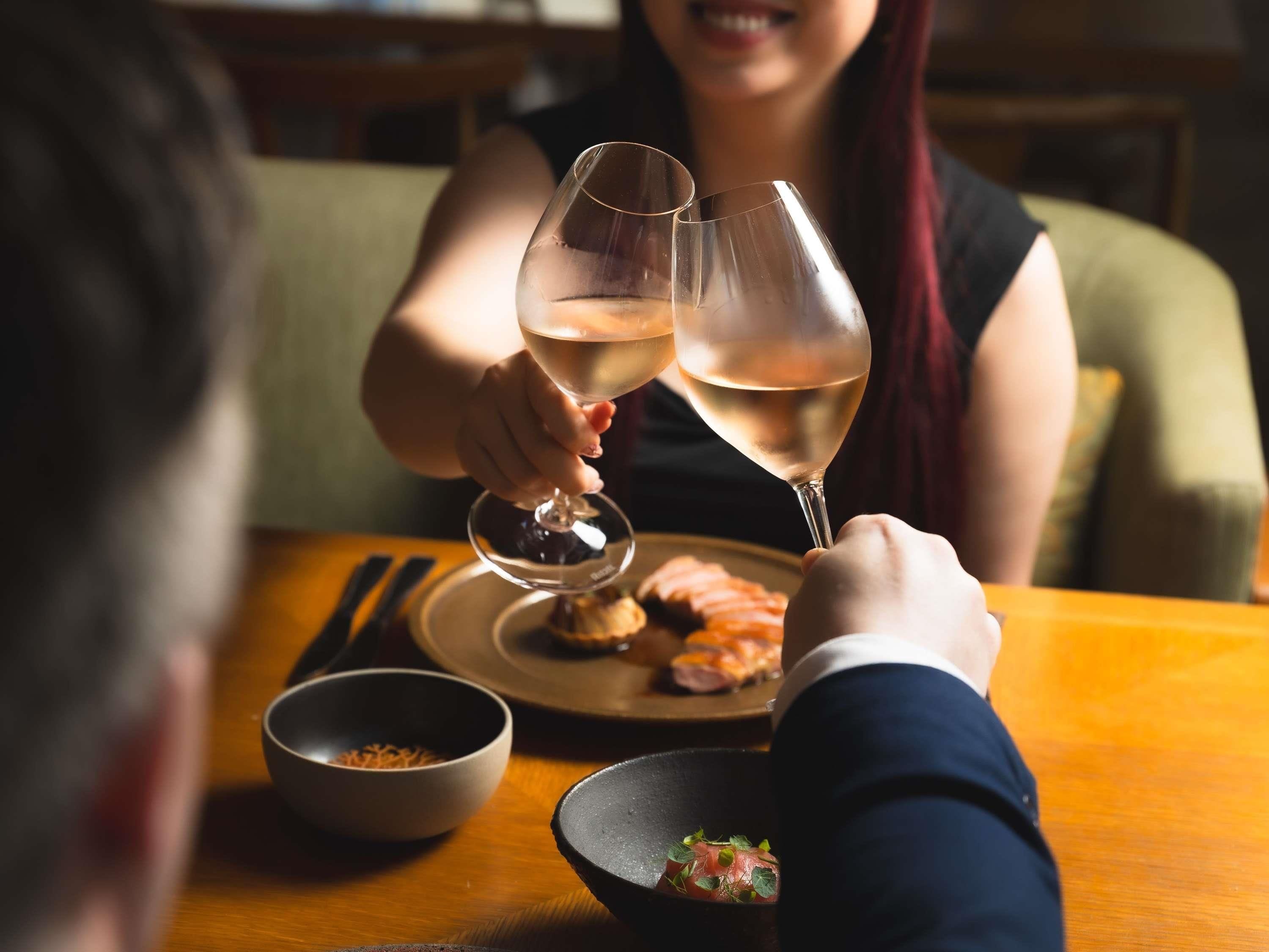 A dining table with a plate of food, a bowl, and two wine glasses.