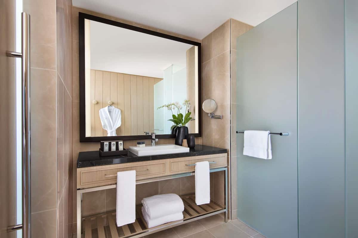 A modern bathroom with a large mirror, a sink, a towel rack, and a shower area.