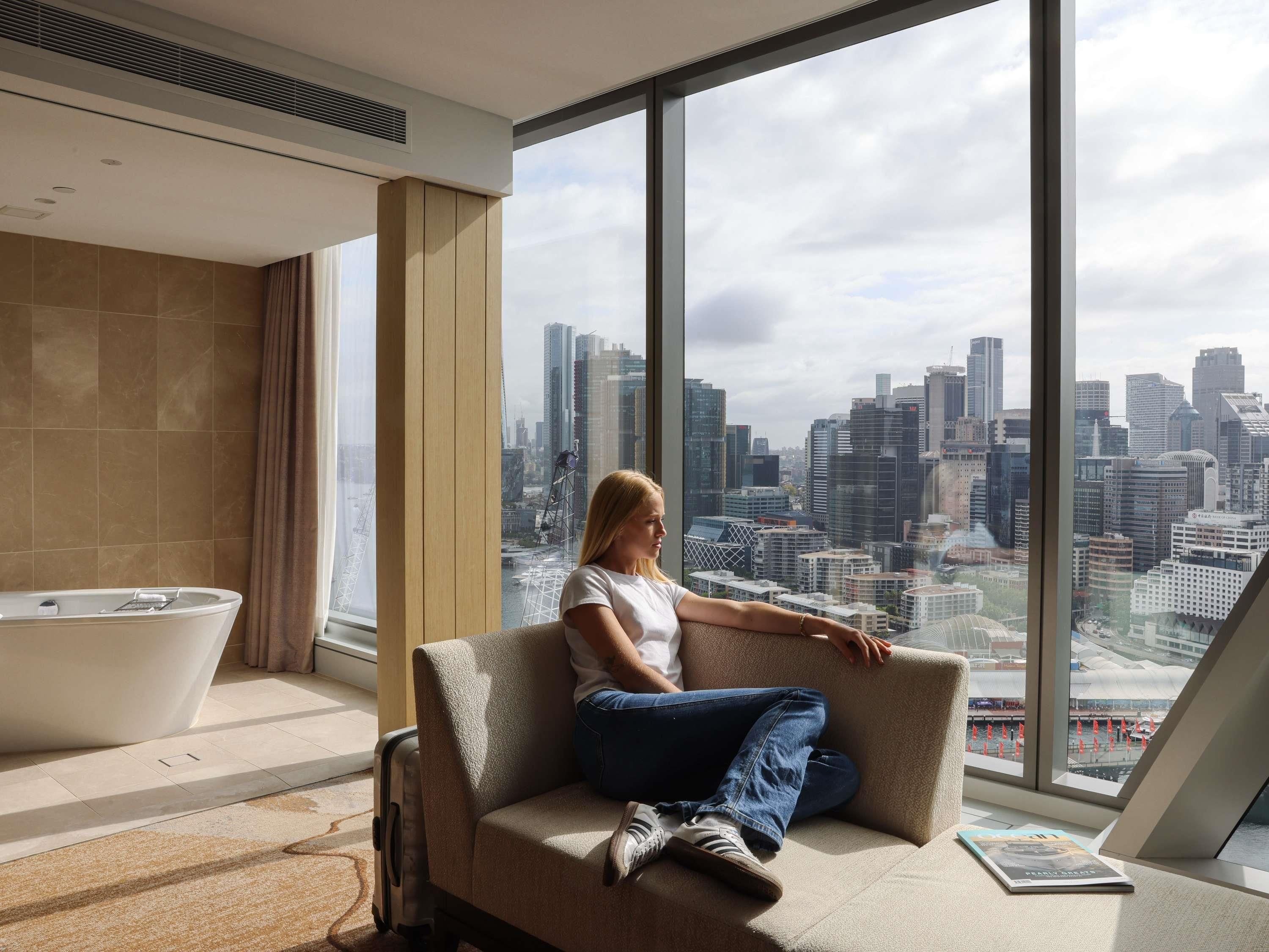 A modern hotel room with a large window, a bathtub, and a city view.