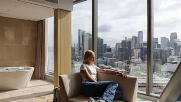 A modern hotel room with a large window, a bathtub, and a city view.