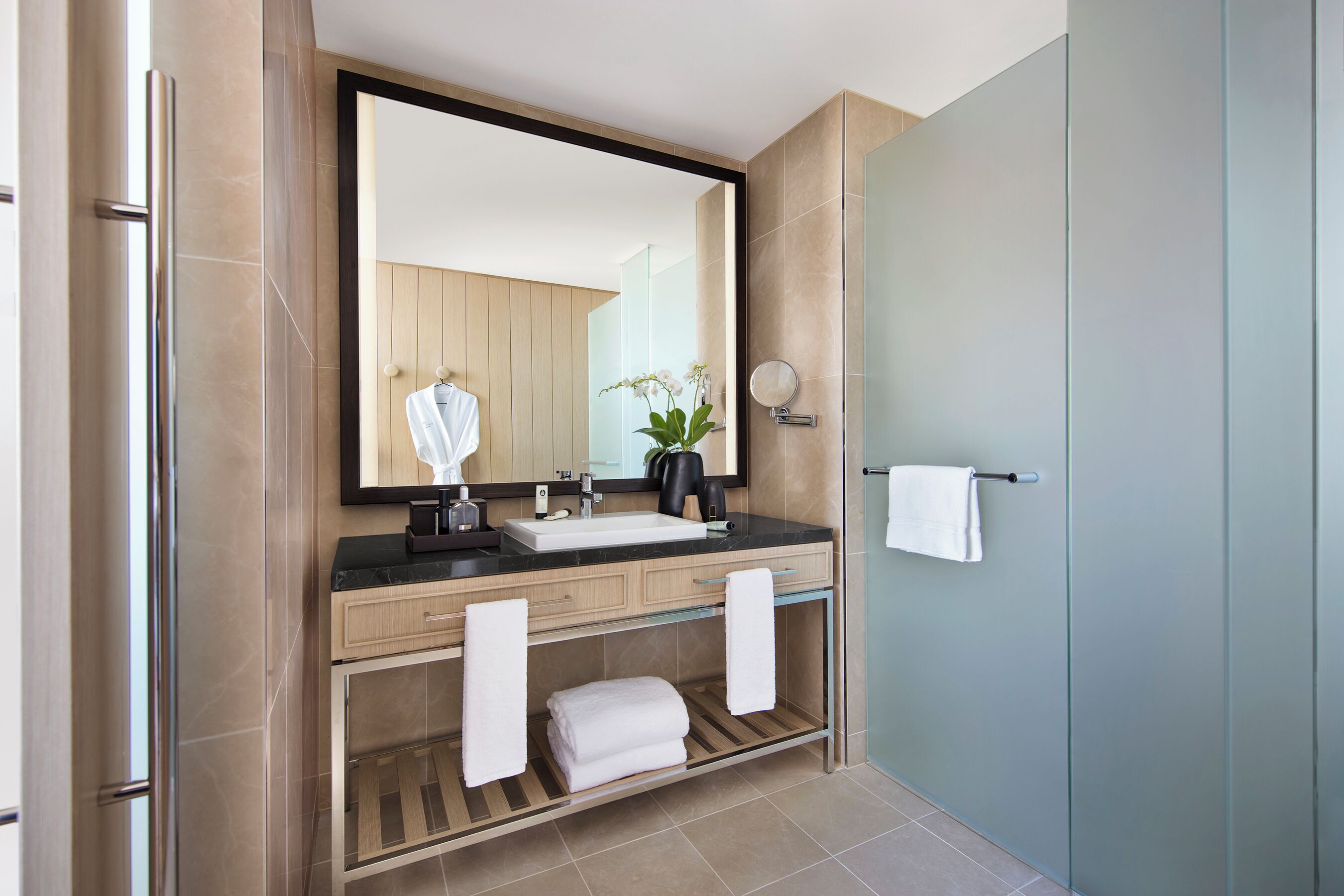A modern bathroom with a large mirror, a sink, a towel rack, and a shower area.