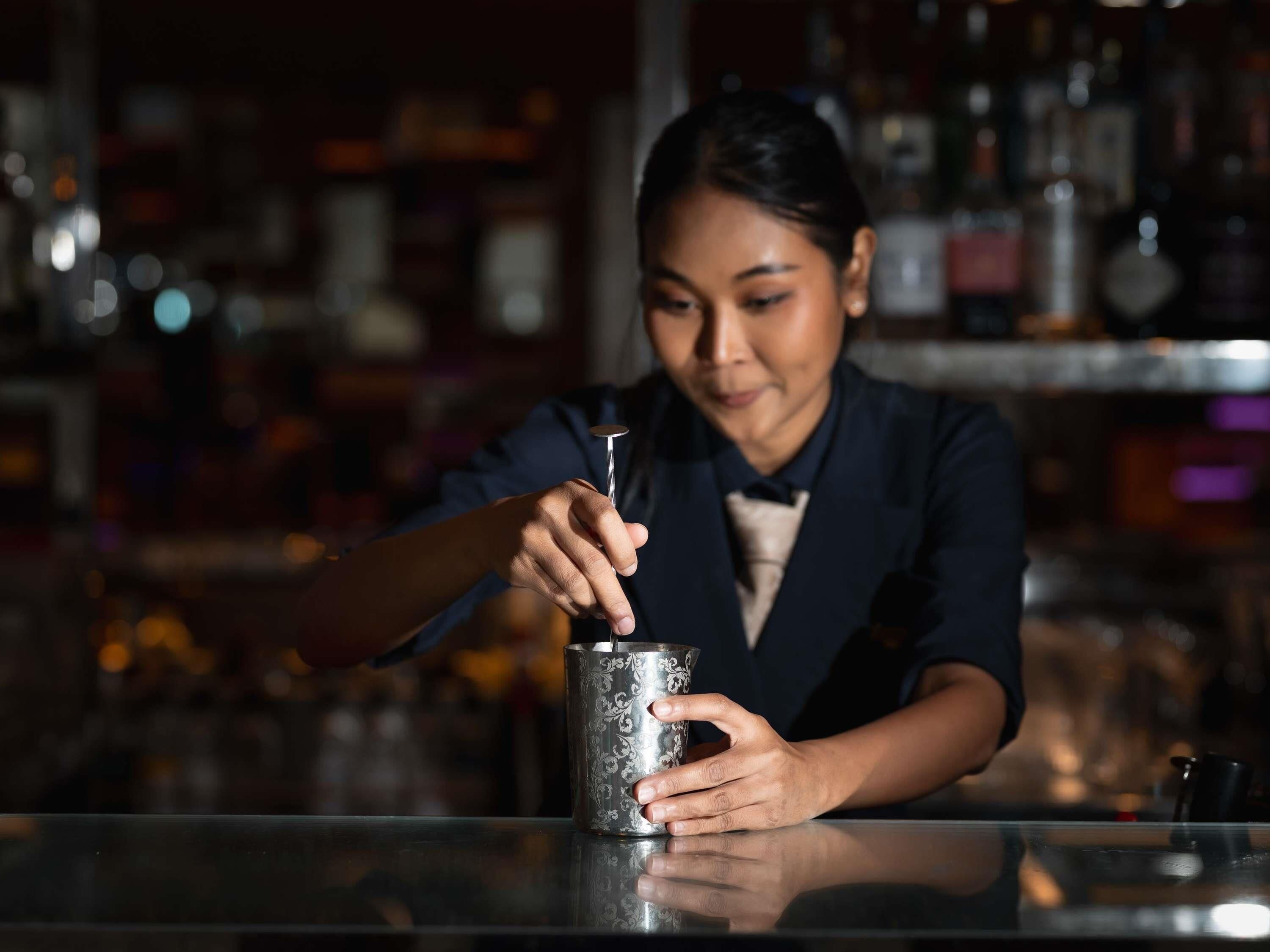 A person pouring a drink into a metallic mug at a bar.