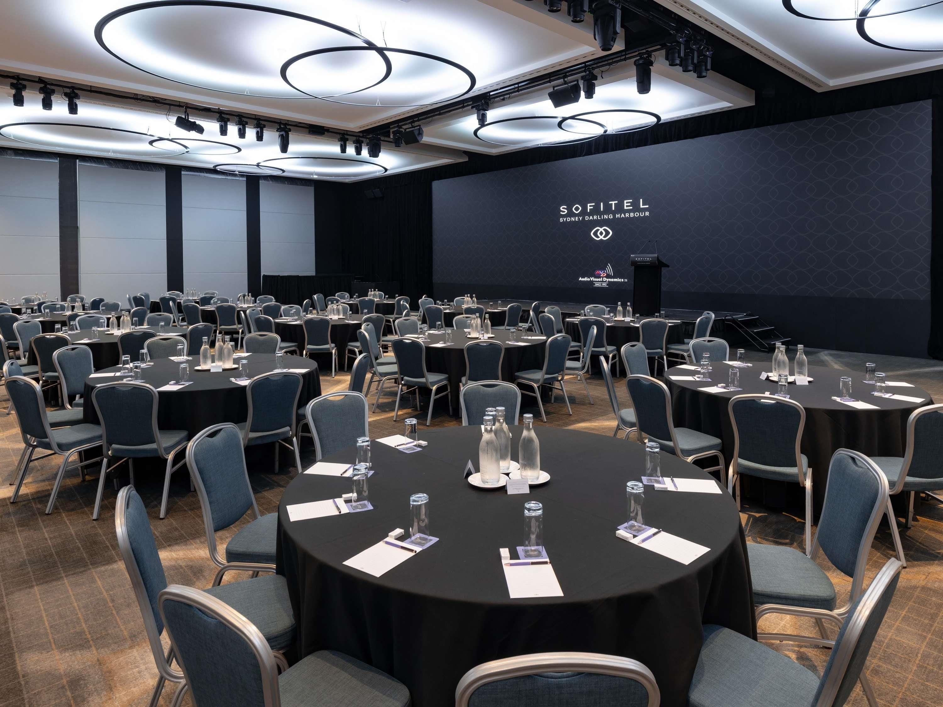 Een congreszaal met ronde tafels, stoelen en een podium.