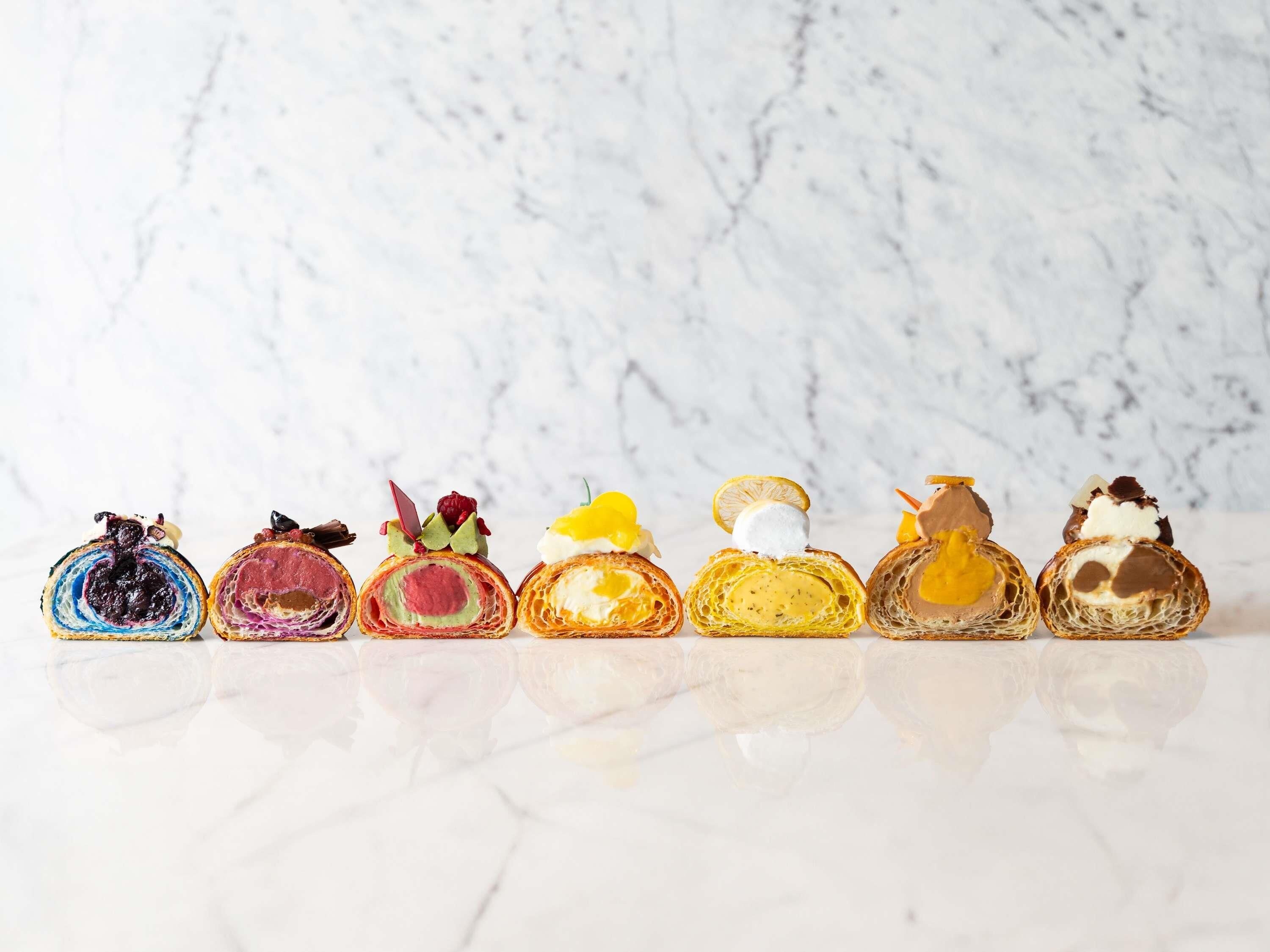 A row of six pastries on a reflective surface with a marble background.