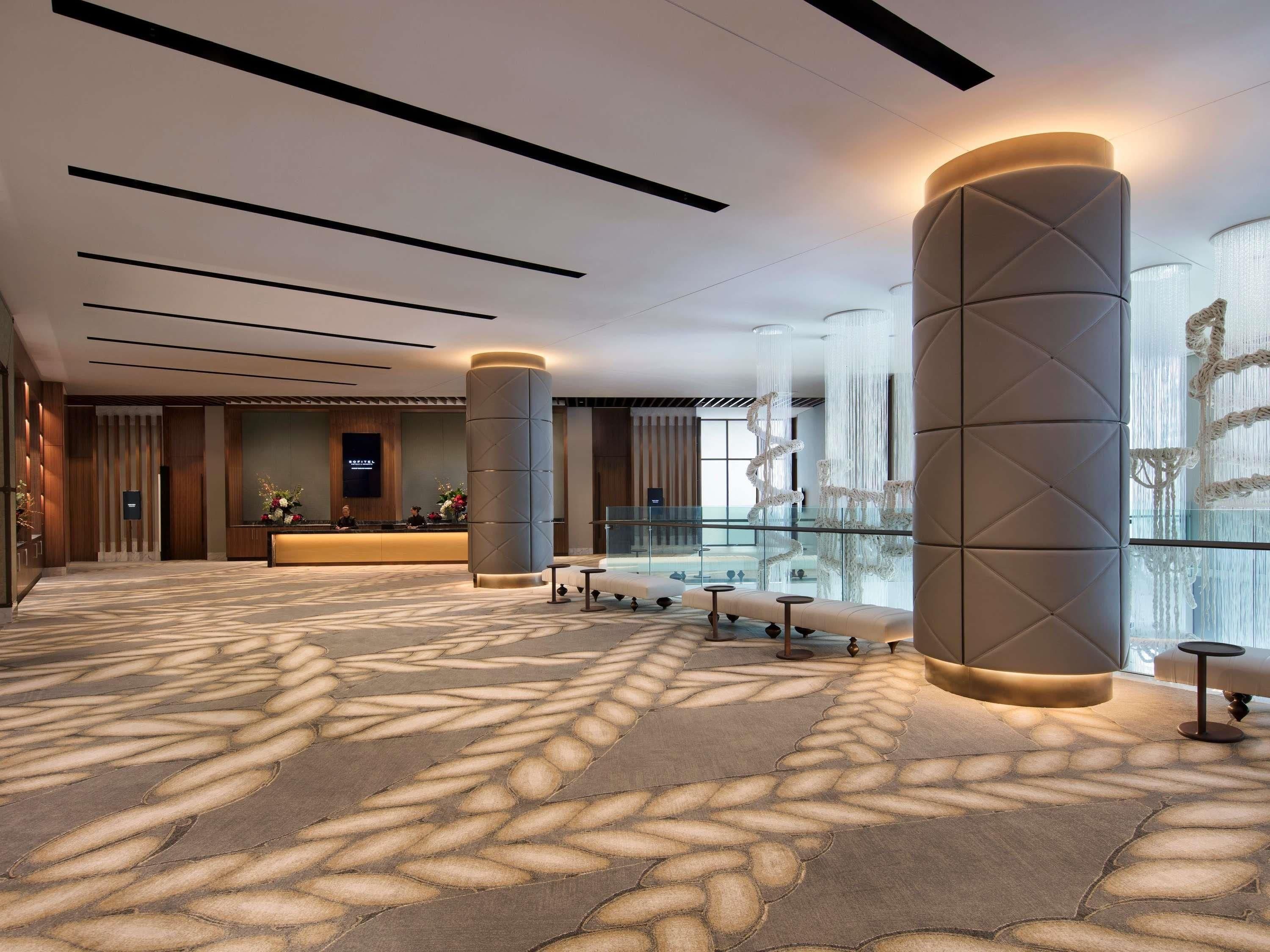 A modern hotel lobby with a reception desk, seating area, and large decorative columns.