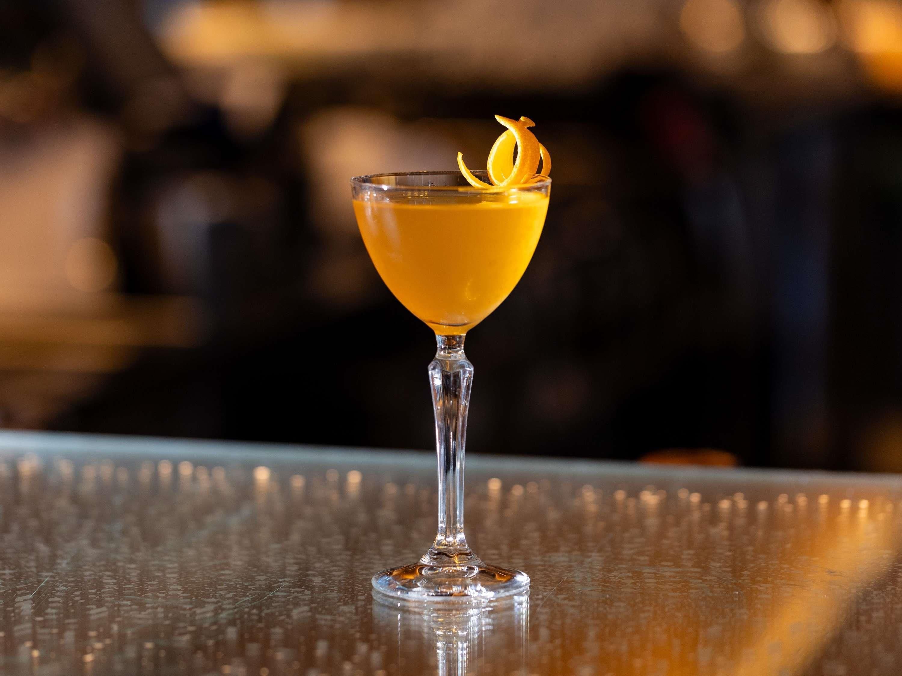 A cocktail in a stemmed glass with a garnish on a reflective surface.