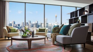 Una sala de estar moderna con vista a la ciudad, que incluye una mesa redonda, dos sillones, un sofá y una estantería.