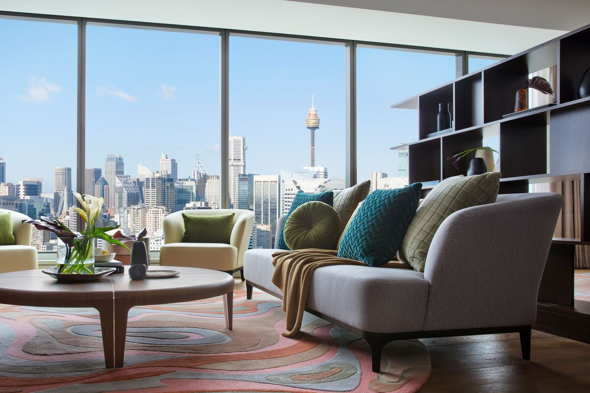 Una sala de estar moderna con vista a la ciudad, que incluye una mesa redonda, dos sillones, un sofá y una estantería.