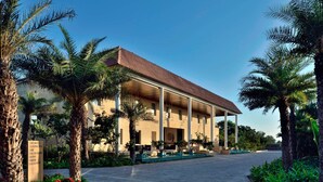 Un hotel con un área exterior techada, palmeras y un sendero pavimentado.