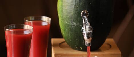 Une table en bois avec un robinet en métal qui verse un liquide rouge dans un verre, et deux autres verres remplis du même liquide.