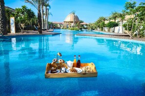 A pool with a wooden tray of breakfast items, including pastries, a jug of juice, and a bottle of water. - The Westin Pushkar Resort & Spa (Peesangan)