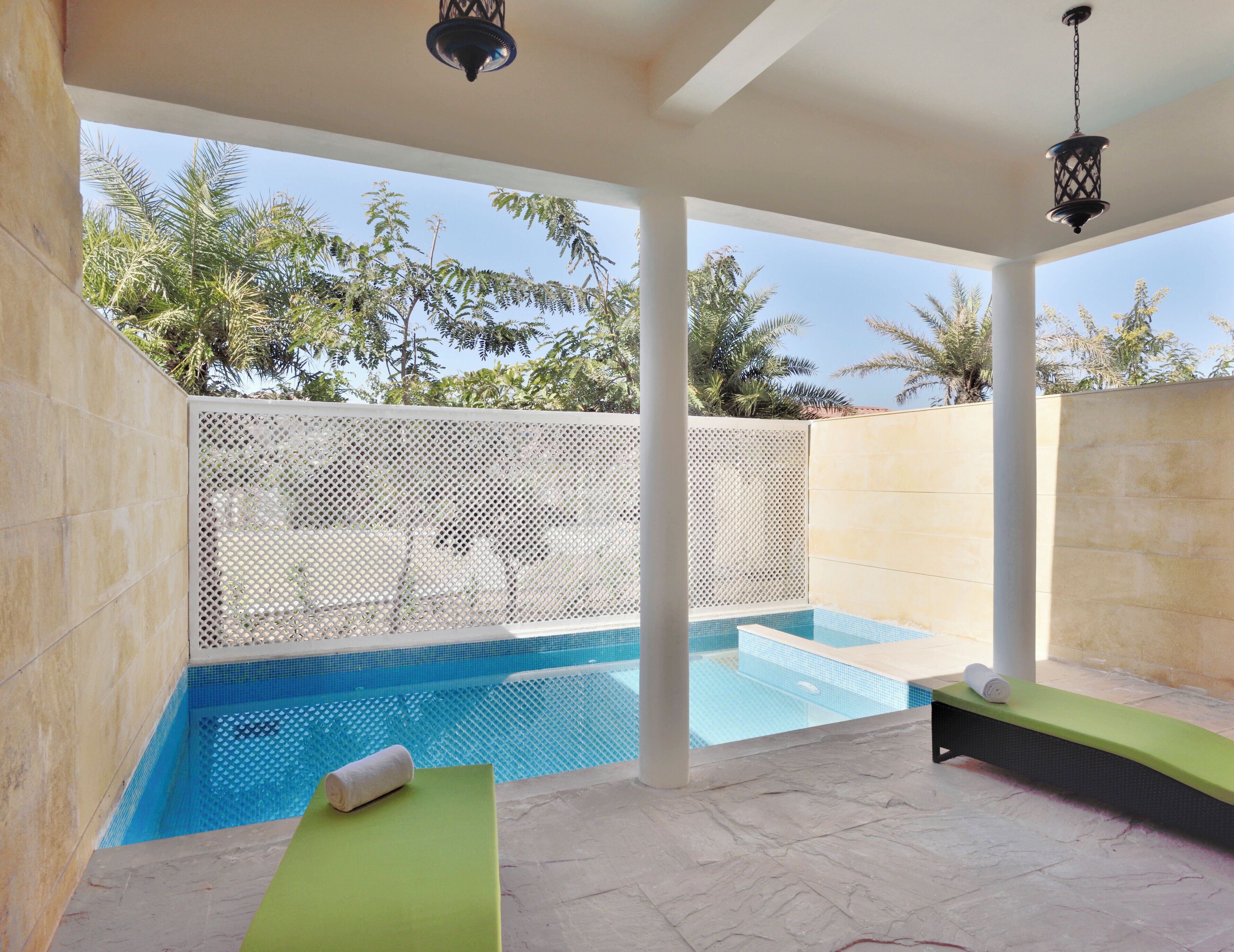 A pool area with a clear view of the pool, a green lounge chair, a white towel, and a hanging lantern.