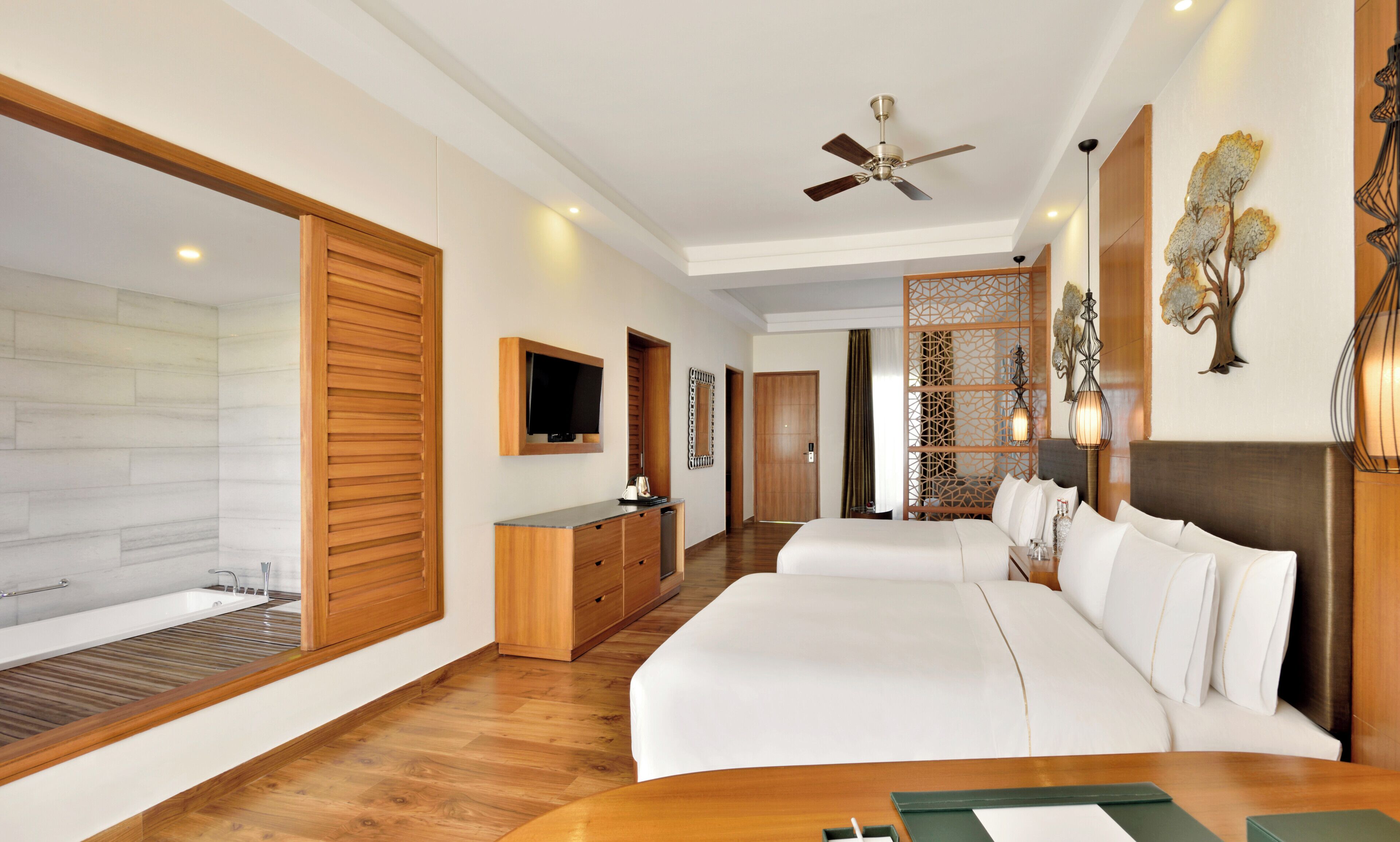Quarto de hotel com uma cama grande, televisão, cómoda de madeira, casa de banho com banheira e um painel decorativo na parede.