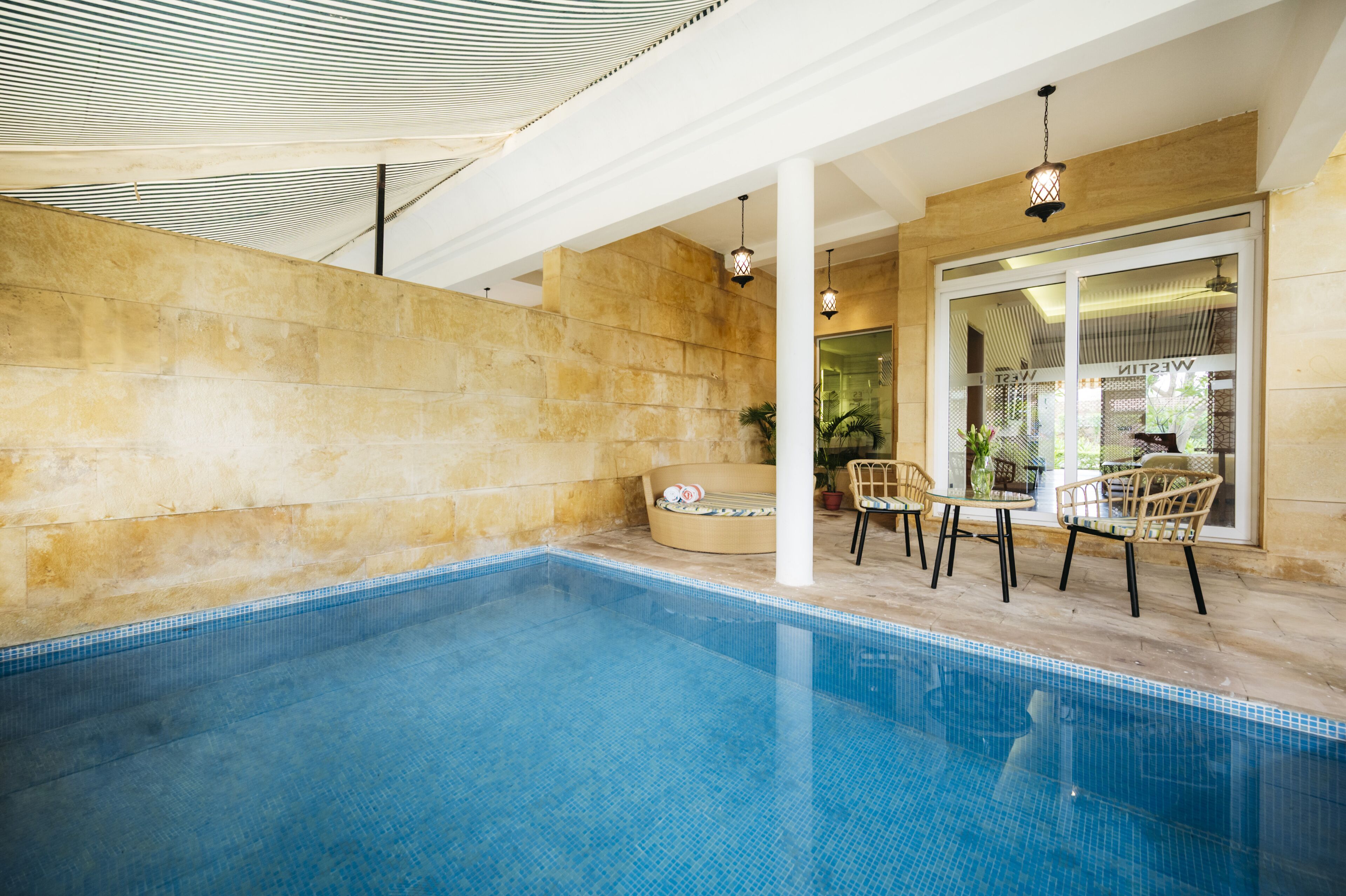 A swimming pool with a tiled floor, surrounded by stone walls and wicker furniture.