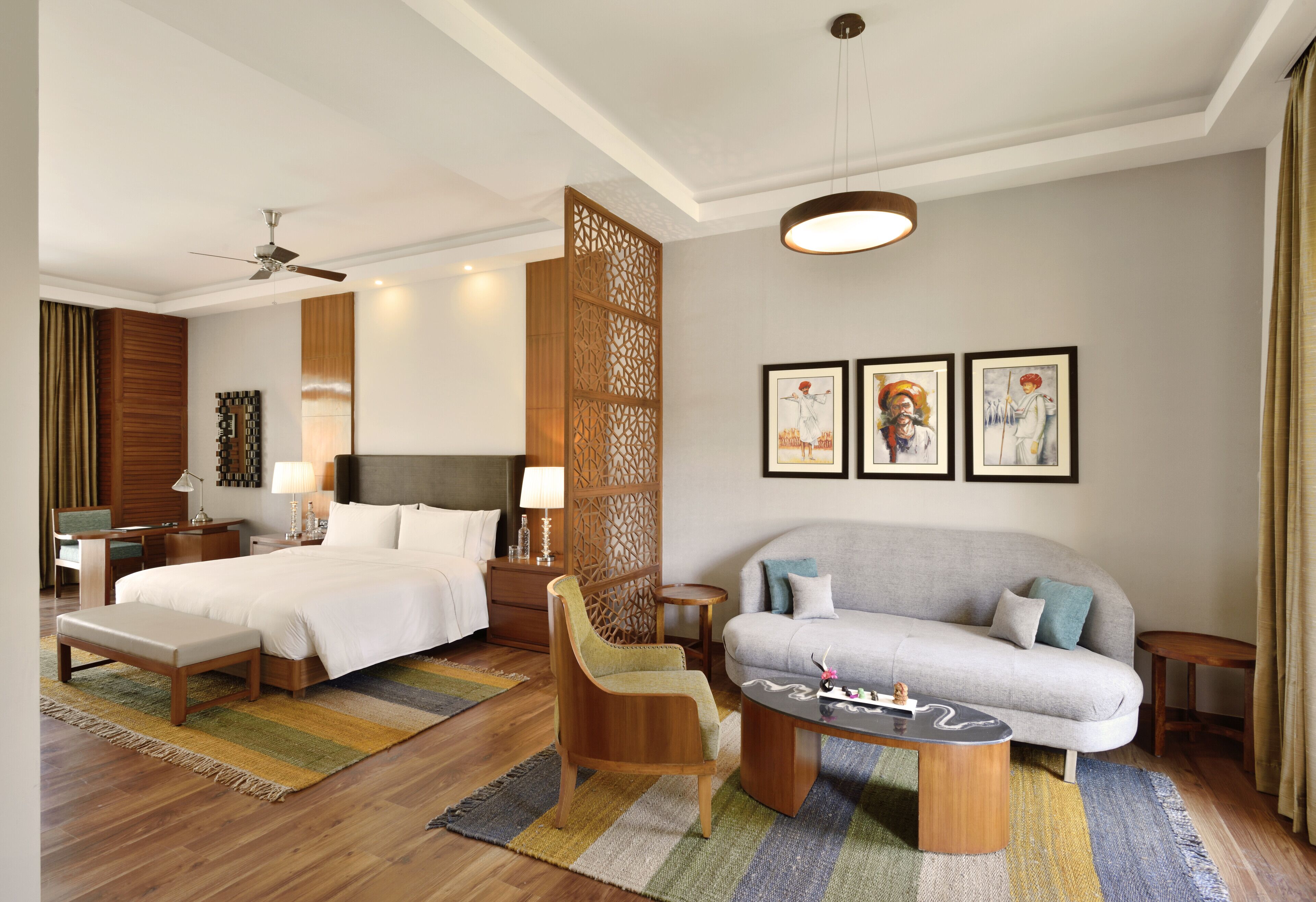 A hotel room with a bed, a sofa, a chair, a coffee table, a desk, and a lamp.