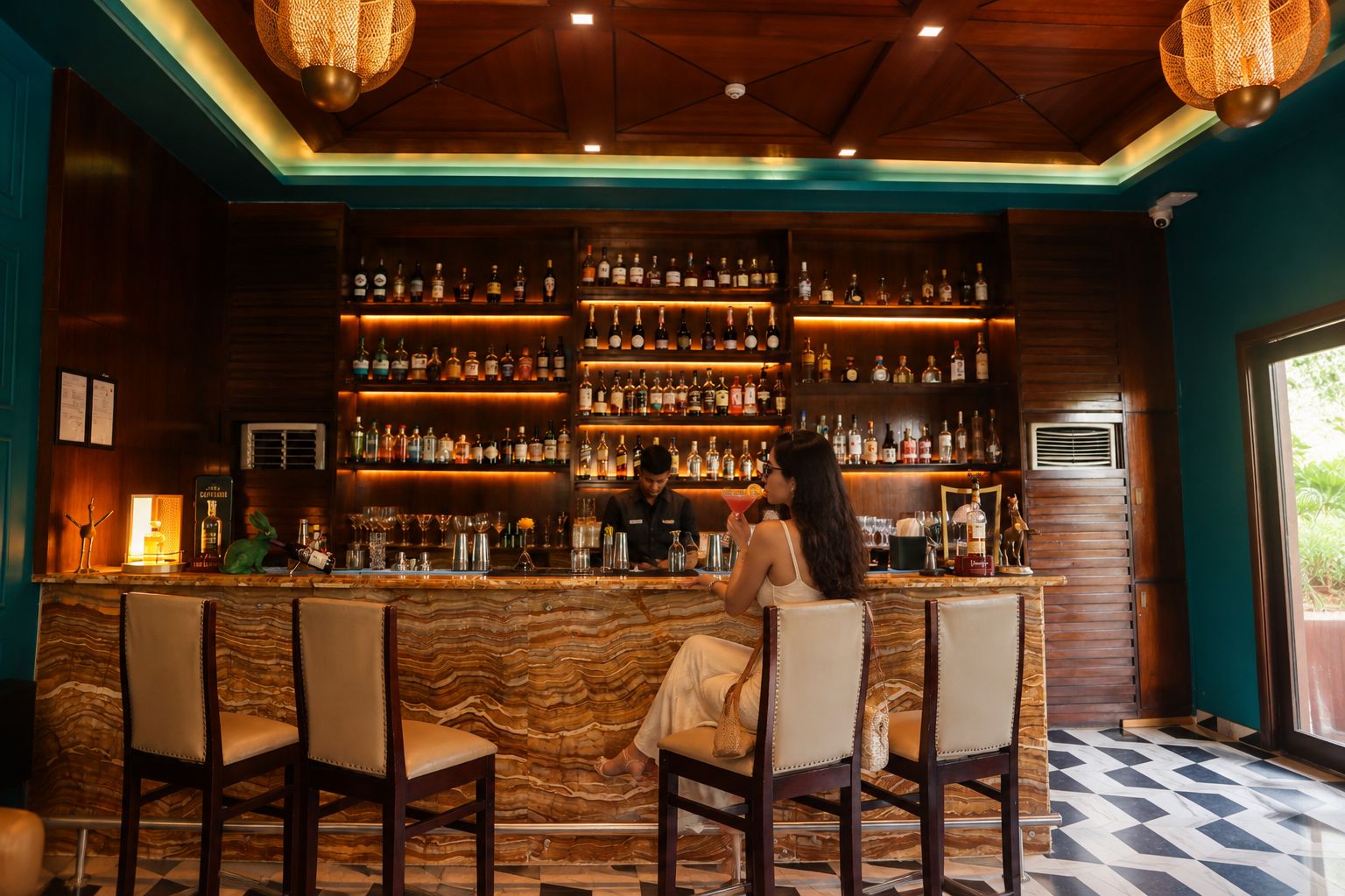 Una zona de bar con mostrador de mármol, varias estanterías llenas de botellas y taburetes.