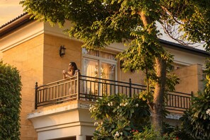 Un edificio residencial con balcón, una ventana con cortinas y un árbol en primer plano.