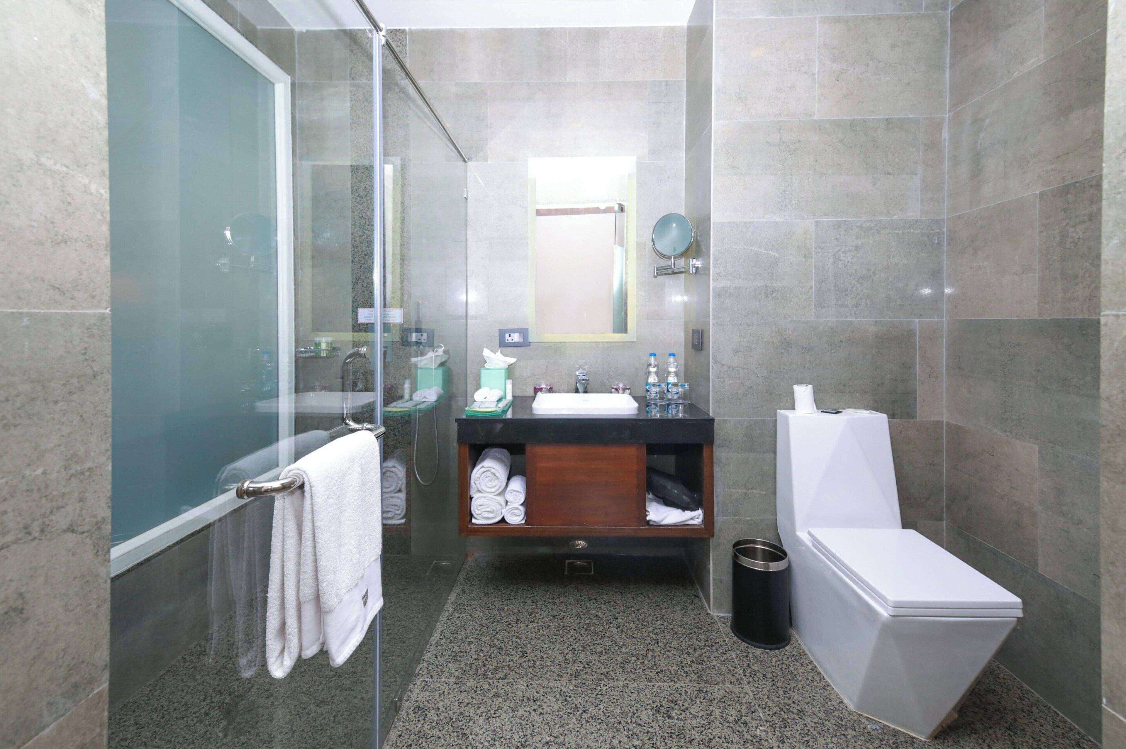 Et moderne badeværelse med en glasbrusekabine, et trækommode, et hvidt toilet og et stengulv af granit.