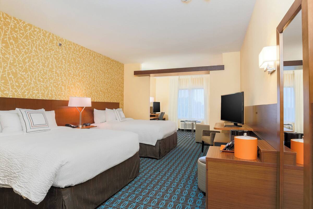 A hotel room with two beds, a desk with a computer, a TV, and a bathroom mirror.