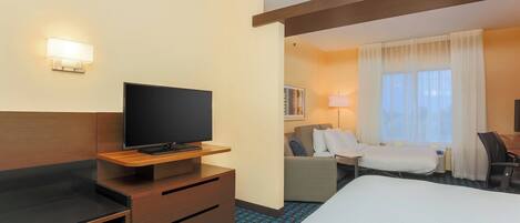 A hotel room with a bed, a desk with a flat-screen TV, a chair, a sofa, and a window with curtains.