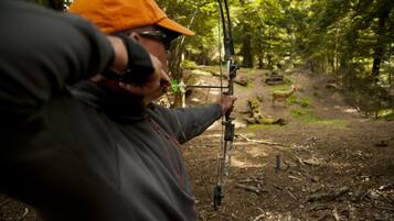 A person aiming a bow in a forest setting.