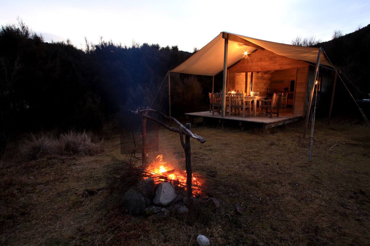 Ein Zelt mit Feuer davor, umgeben von einer Wiese und Bäumen.