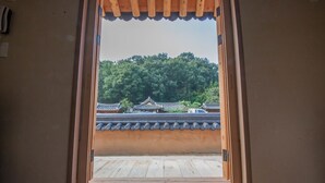 A traditional Japanese room with tatami flooring, a shoji screen door, and a view of a temple with a tiled roof. - Jiwoodang (Jeonju)