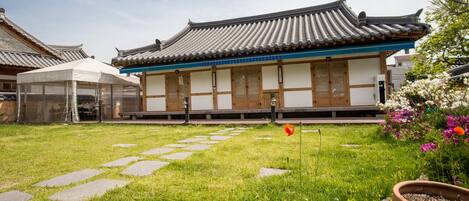 A traditional building with a tiled roof and wooden doors, surrounded by a grassy area with stepping stones and potted plants.
