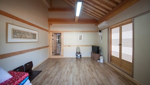 A room with wooden flooring, a bed with a red and white bedspread, a television, and a sliding door with a traditional design. - Jiwoodang (Jeonju)
