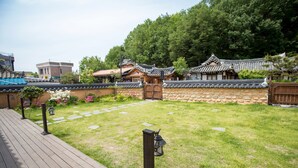 A traditional Korean-style courtyard with stone walls, wooden gates, and a wooden deck. - Jiwoodang (Jeonju)