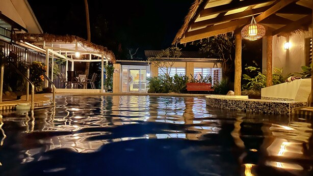 A nighttime swimming pool with a thatched roof structure, a covered seating area, and a well-lit entrance. - Bua Bed & Breakfast (Nadi)