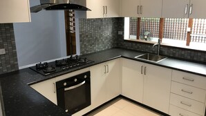 A modern kitchen with white cabinets, a black countertop, a stainless steel sink, and a built-in oven. - Bua Bed & Breakfast (Nadi)
