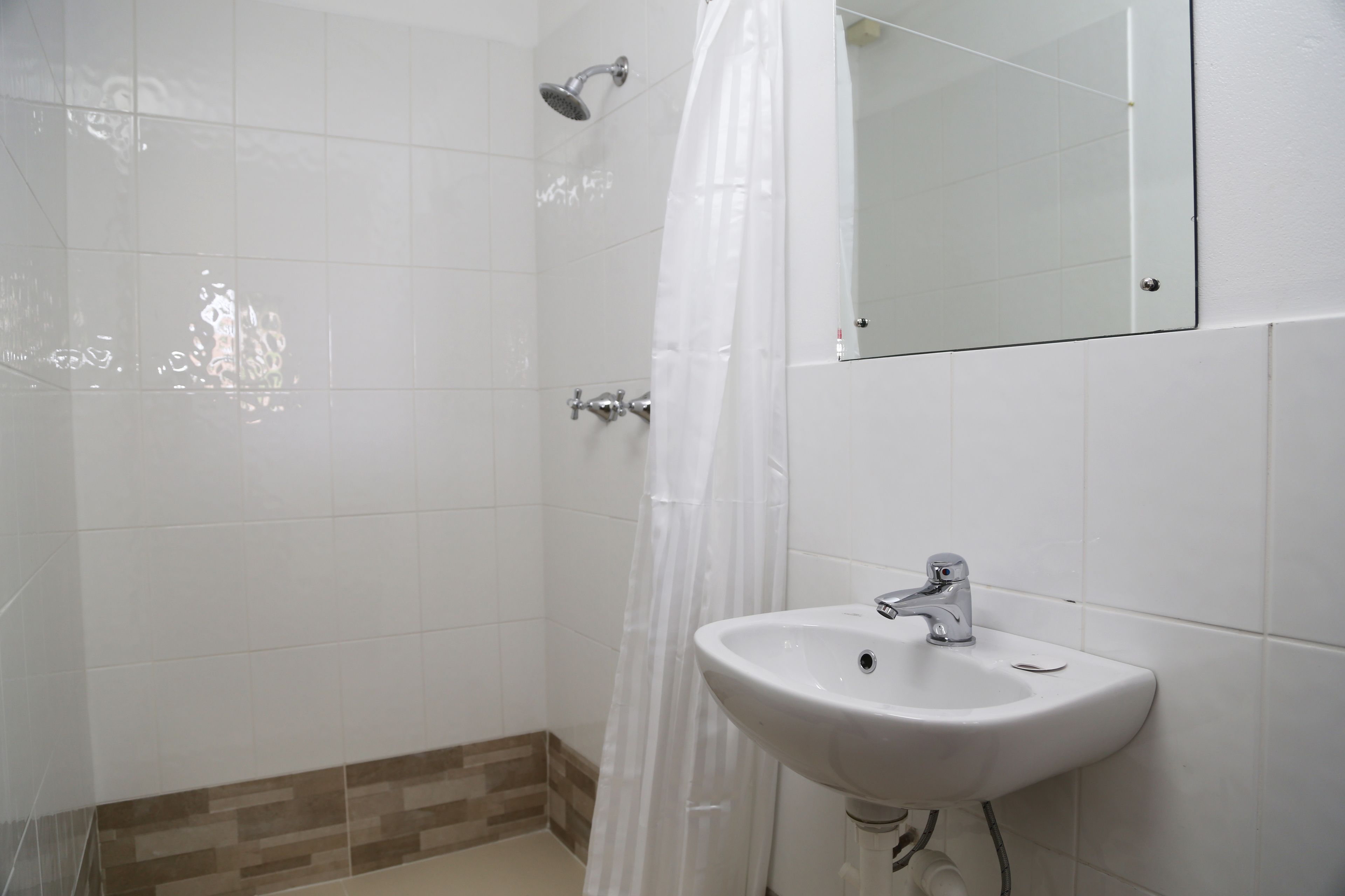 A bathroom with white tiles, a shower, a sink, and a mirror.