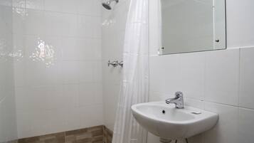 A bathroom with white tiles, a shower, a sink, and a mirror.