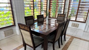A dining area with a glass-top table surrounded by wooden chairs with cushioned backs. - Bua Bed & Breakfast (Nadi)