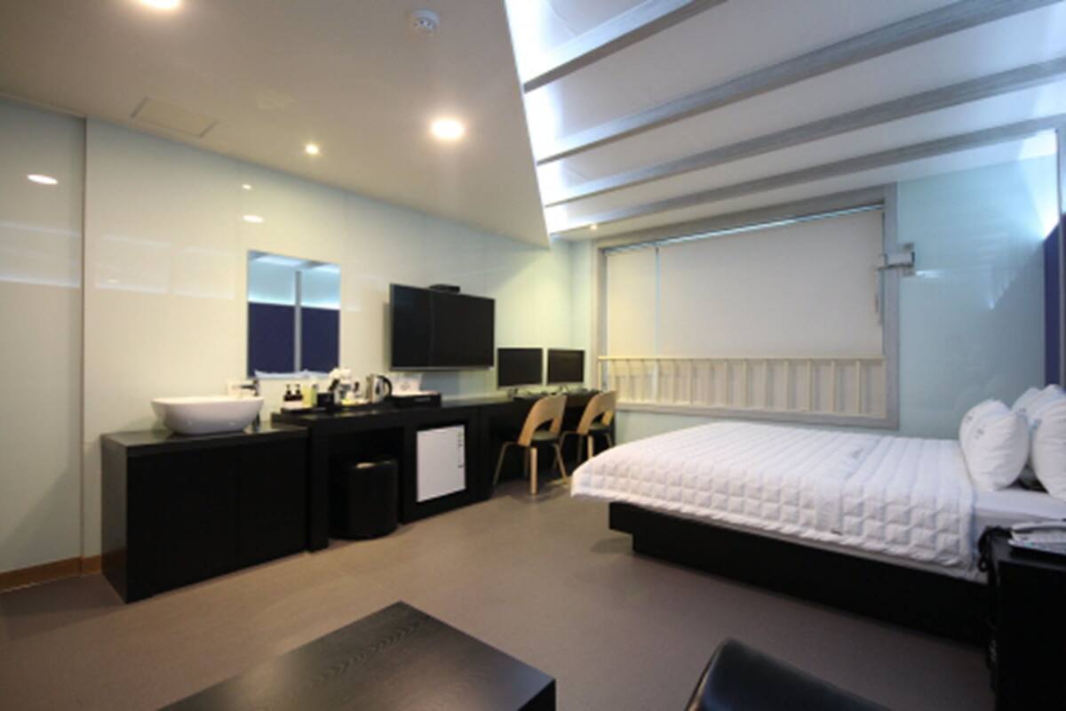 A modern hotel room with a large bed, a desk with a computer, a sink, and a television.