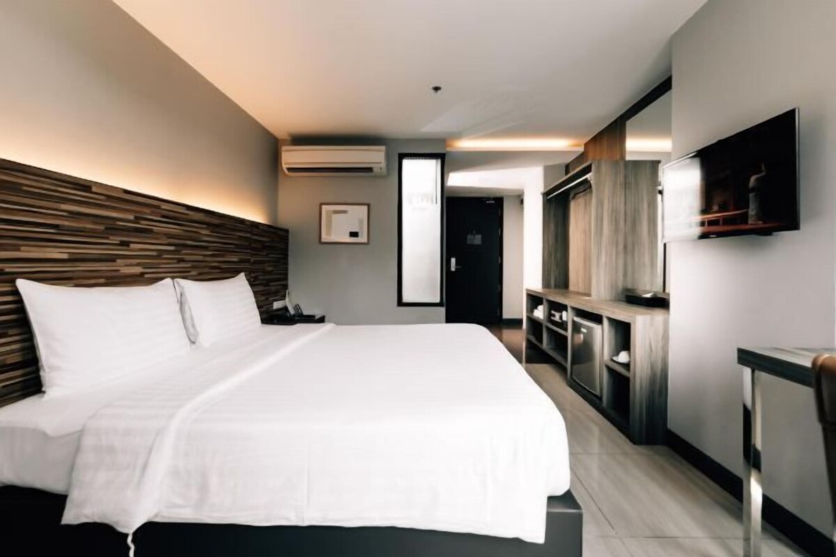 Une chambre d’hôtel moderne avec un grand lit, un téléviseur fixé au mur et une tête de lit en bois.