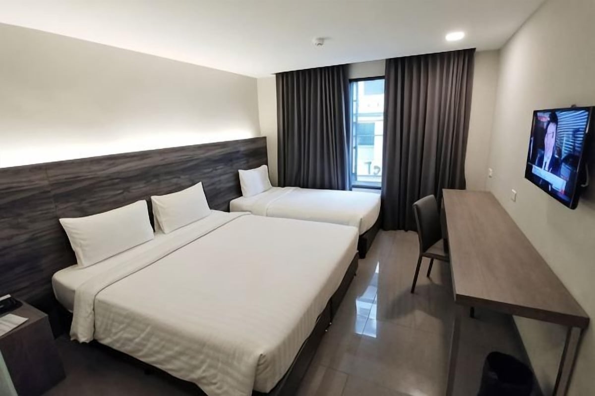 A hotel room with two beds, a desk, a chair, a TV, and a window with curtains.