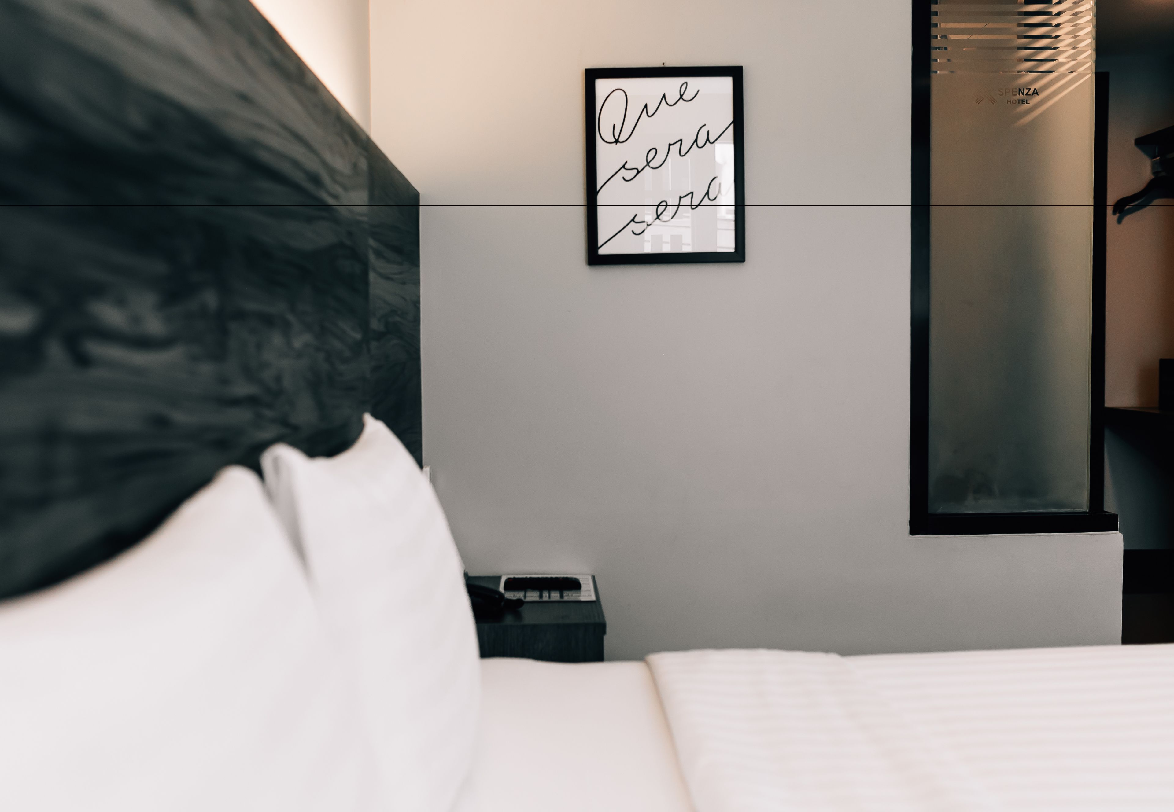 A modern hotel room with a bed, a headboard, a bedside table, a nightstand, a framed sign, and a mirror.