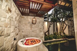 A stone-walled bathroom with a freestanding bathtub, a hanging light fixture, and a small pool area with plants. - Aksari Villa Seminyak by Ini Vie Hospitality (Seminyak)