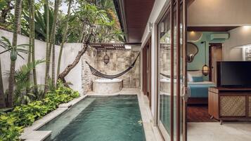 A modern outdoor pool area with a hot tub, surrounded by lush tropical plants and a stone wall.