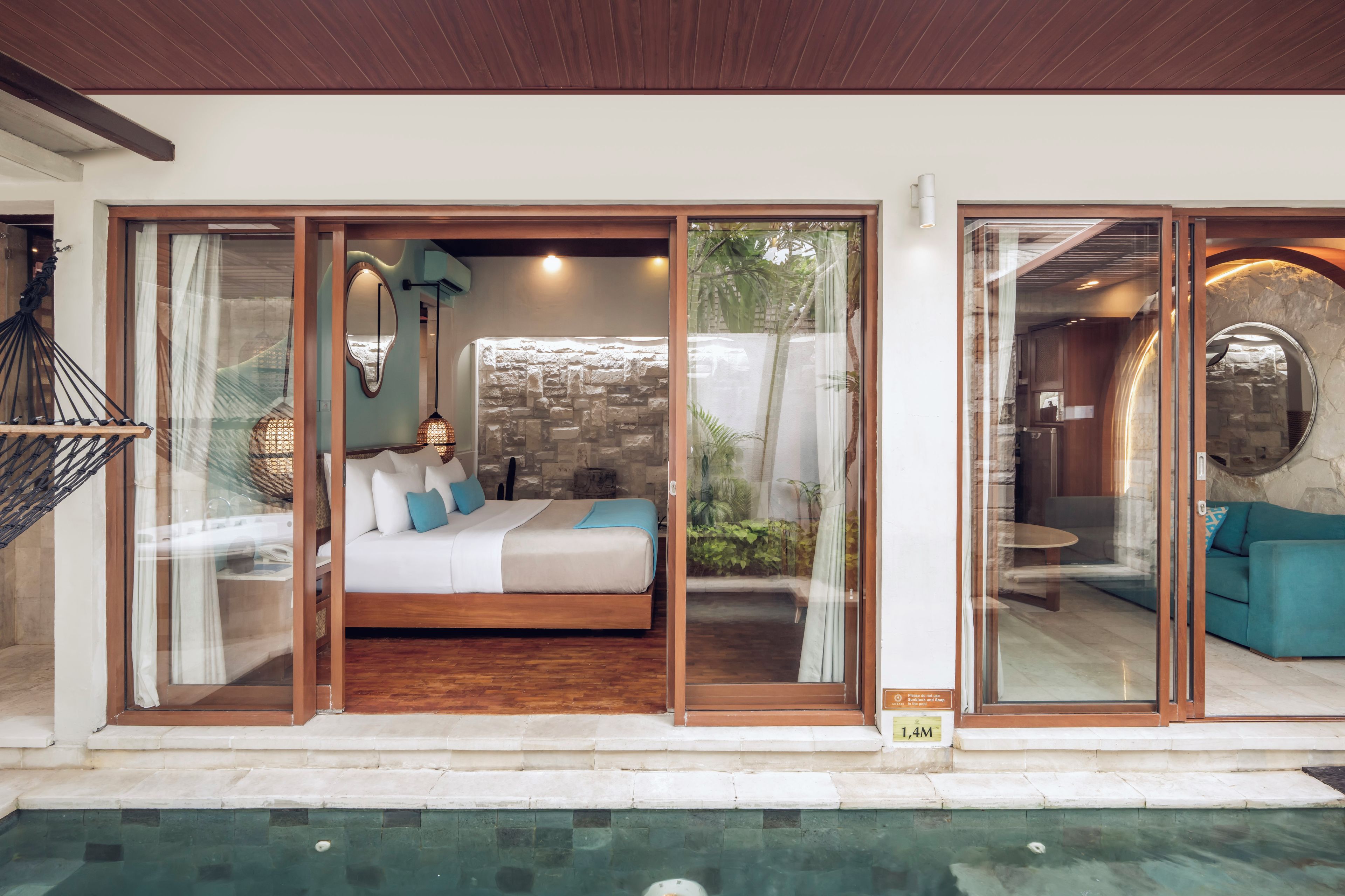 A bedroom with a bed, a glass door leading to a stone wall, and a pool outside.