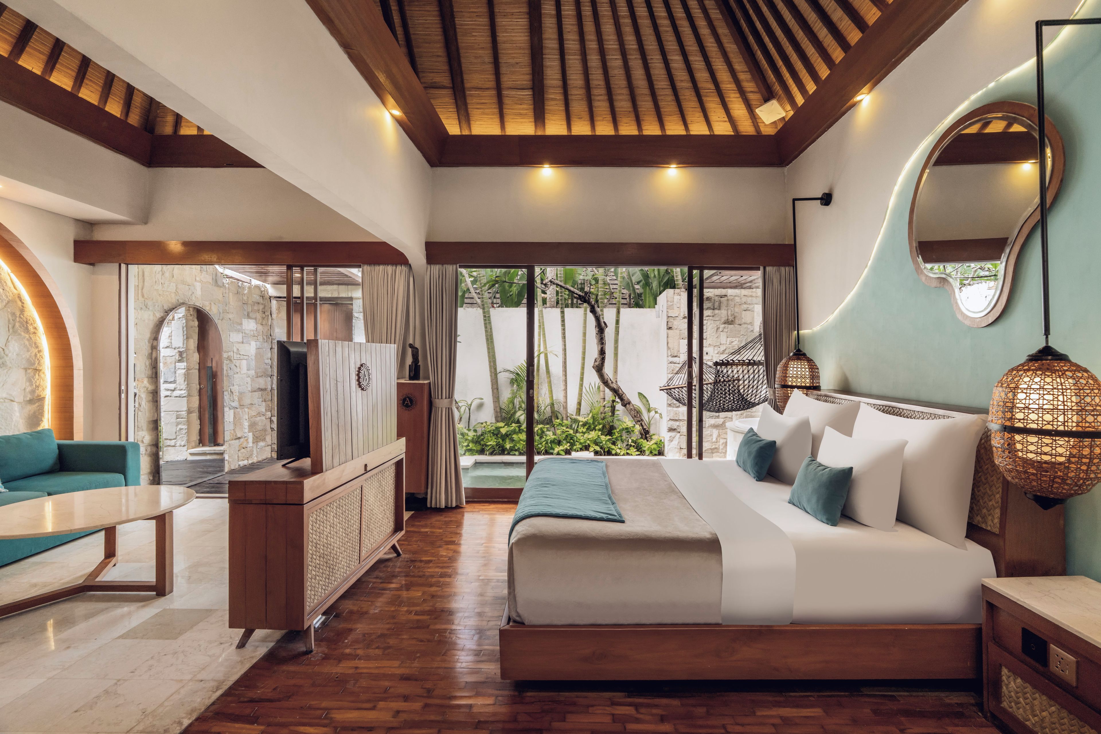 A bedroom with a large bed, a TV, a sofa, and a stone wall.