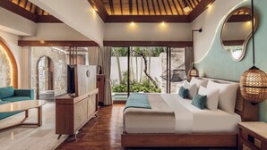 A bedroom with a large bed, a TV, a sofa, and a stone wall. - Aksari Villa Seminyak by Ini Vie Hospitality (Seminyak)