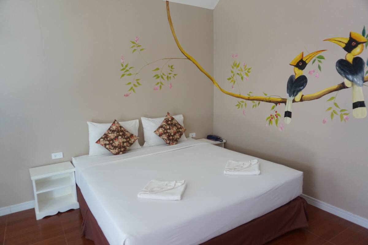 A hotel room with a bed, pillows, a nightstand, and a wall mural of birds on a branch.