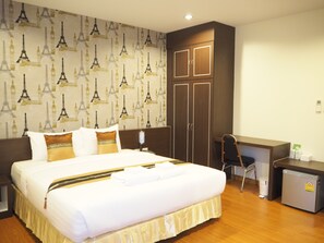 A hotel room with a large bed, a desk, a chair, a small refrigerator, and a wardrobe. - Suksomboon Hotel (Surat Thani)