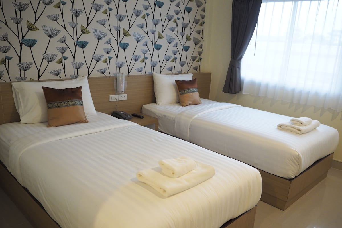 Hotelkamer met twee bedden, elk met witte lakens en kussens, een houten hoofdbord, een nachtkastje met een telefoon en een wand met een bladmotief.