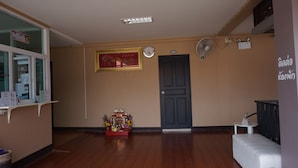 Un área de recepción con piso de madera, mostrador de recepción, un reloj, una puerta con la leyenda '102' y un pequeño santuario con ofrendas.